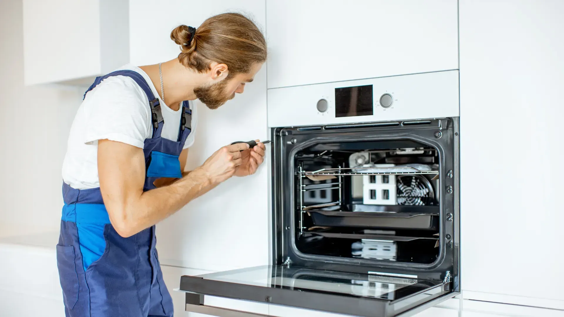 A man is fixing an oven in a kitchen.