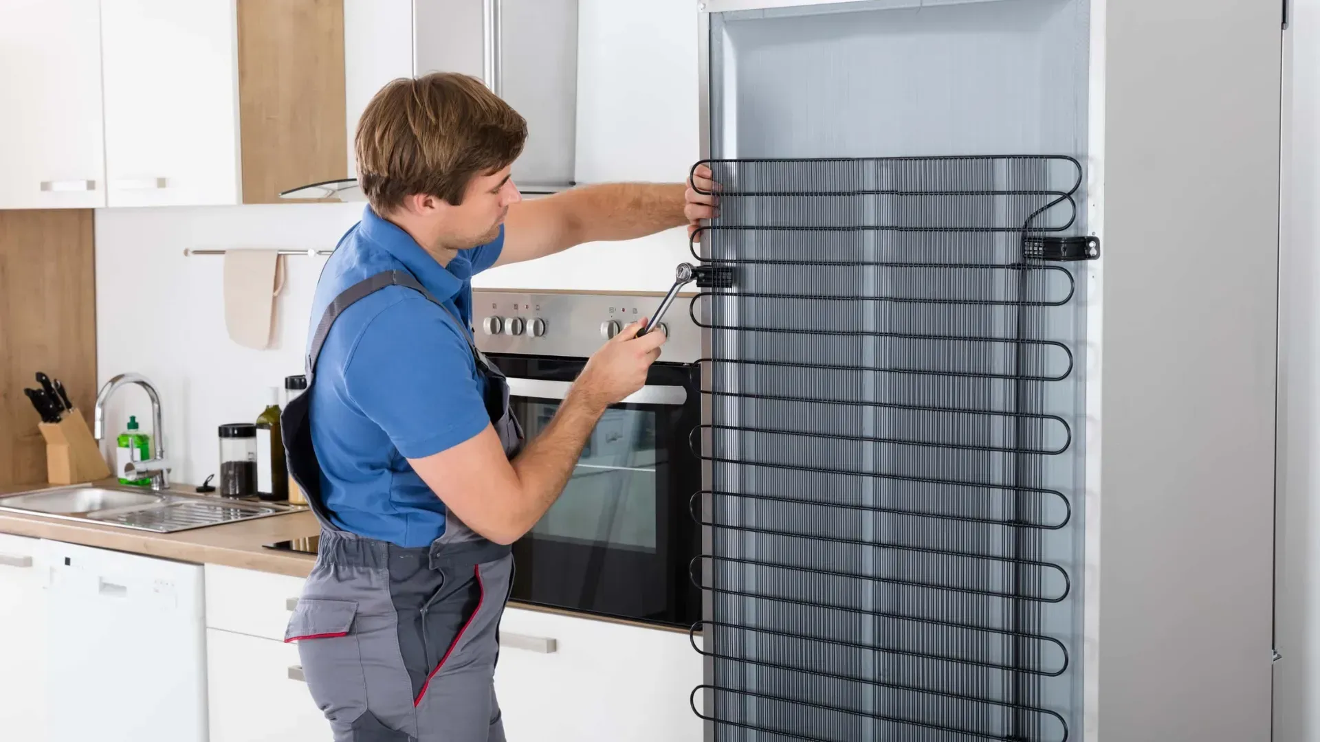 A man is fixing a refrigerator in a kitchen.