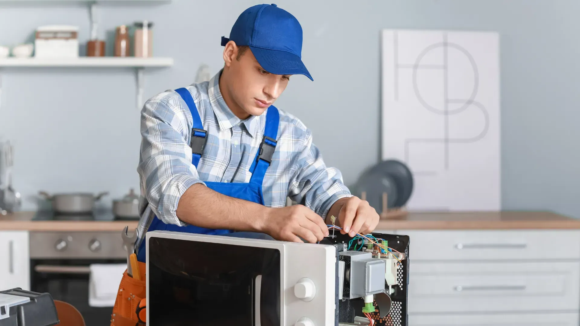 A man is fixing a microwave in a kitchen.
