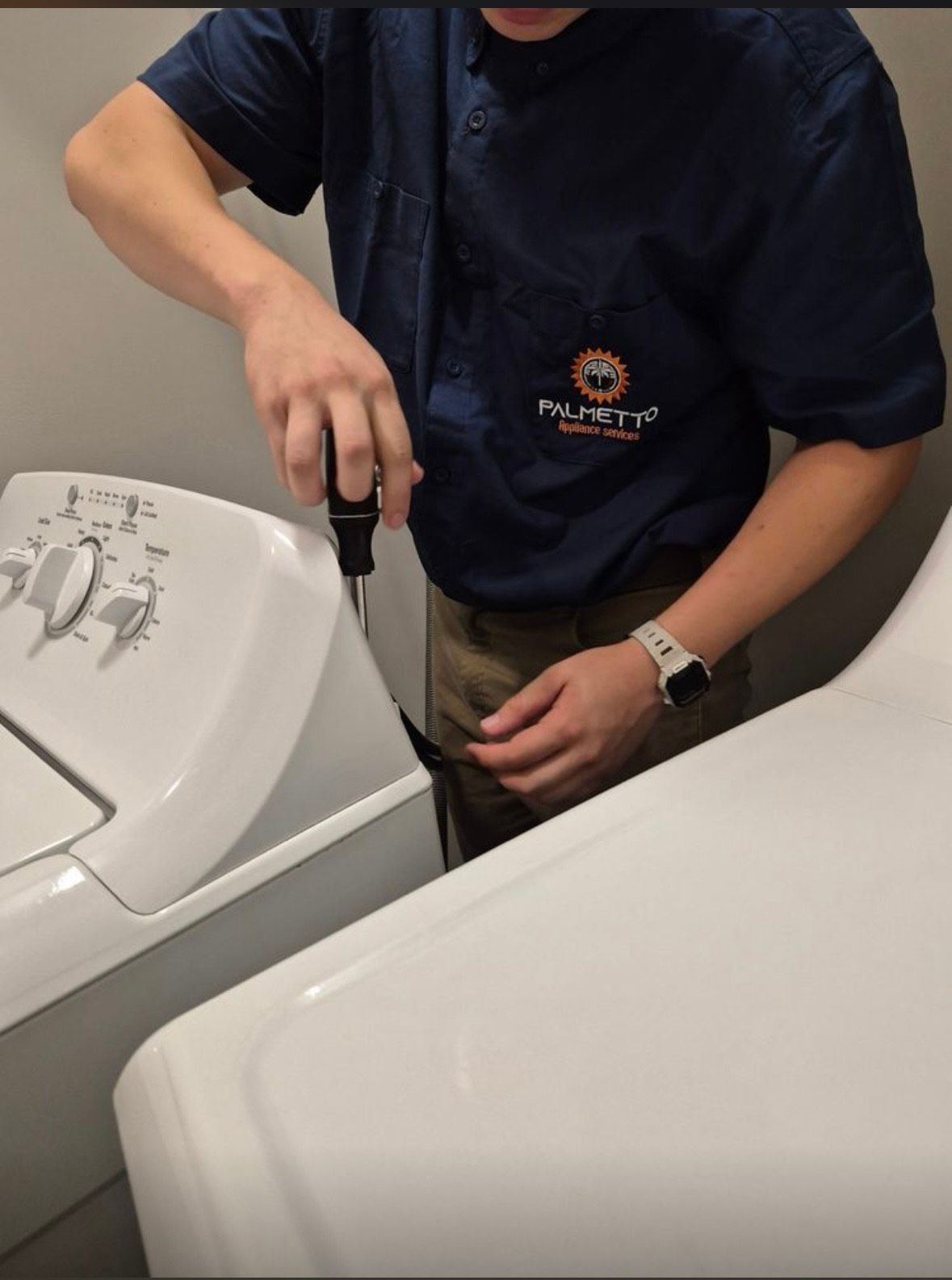 A man wearing a palmetto shirt is working on a washing machine