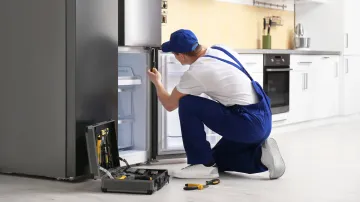 A man is repairing a refrigerator in a kitchen.