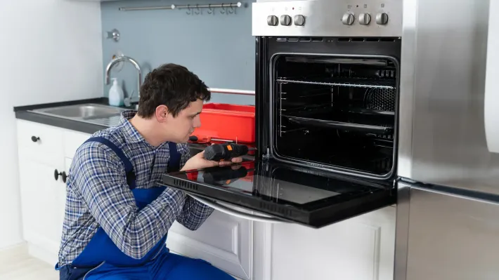 A man is fixing an oven in a kitchen.
