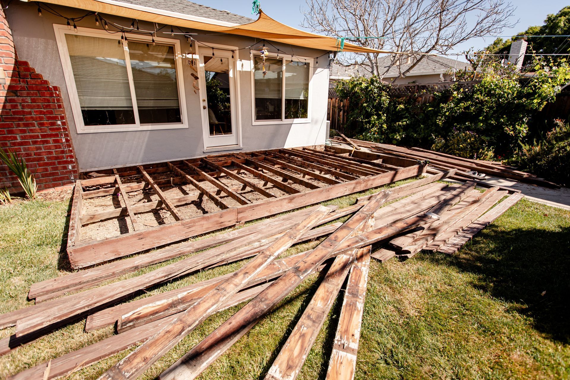 Collapsed wooden deck beside a house, with scattered lumber and a grassy yard.