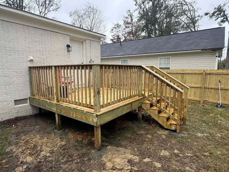 Wooden backyard deck with stairs and railing beside a house, enclosed by a fence.