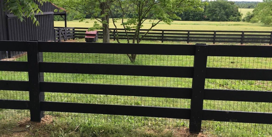 Black wooden fence in a grassy field with trees and a distant farm landscape