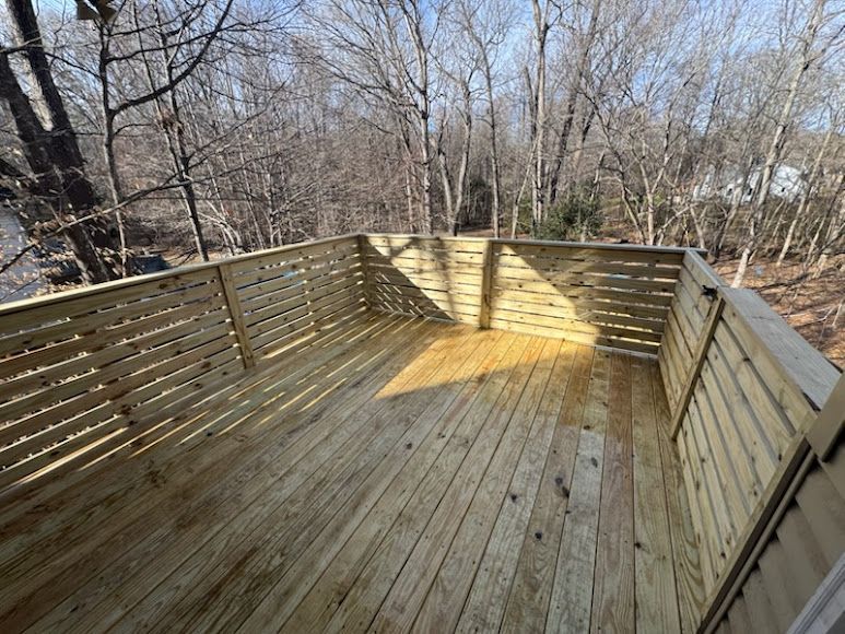 Wooden deck with slatted railing and leafless trees beyond, sun casting a warm patch on the floor