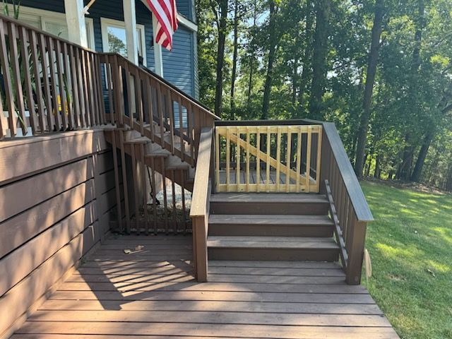 Wooden deck stairs with a railing, leading down to a wooded backyard beside a house.