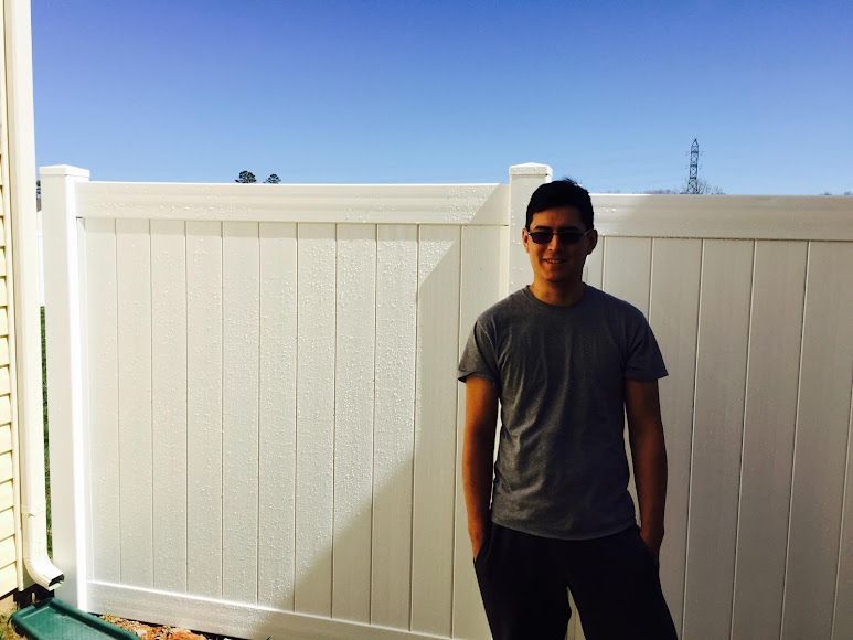 Person in sunglasses standing by a white fence outdoors under a clear blue sky.