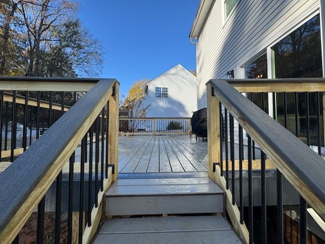 Wooden deck steps leading to a snowy yard and white house under a clear blue sky