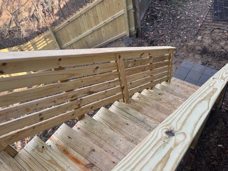 Wooden outdoor stairs descending beside a fenced backyard, viewed from the top.