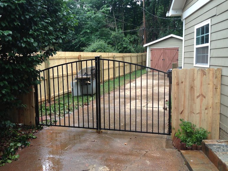 Driveway blocked by a black metal gate with wooden side panels after rain