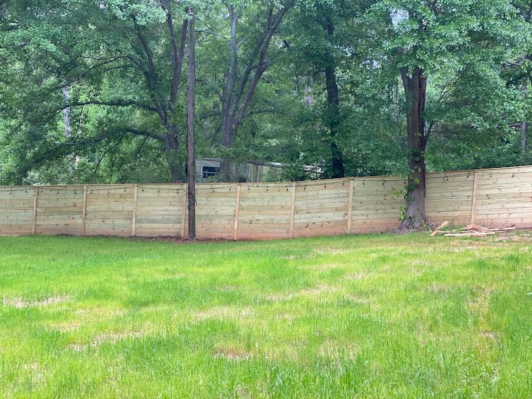Grassy yard bordered by a tan wooden fence and tall green trees
