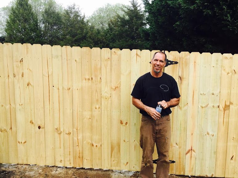 Man standing by a wooden fence, holding a drink in a backyard.