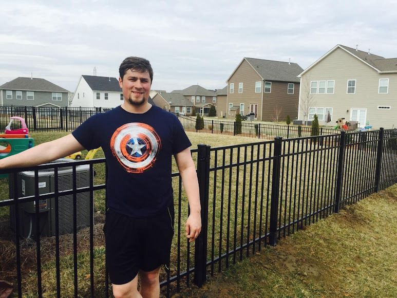 Person in a Captain America shirt standing by a black fence in a suburban neighborhood