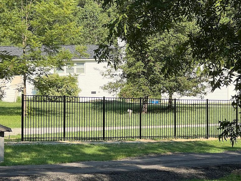 Black metal fence beside a grassy yard with a white house and trees in the background.