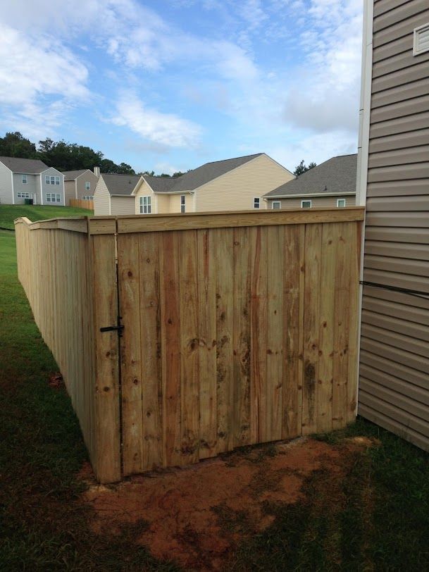 Wooden backyard fence panel beside a house, with a gate and neighboring homes in the background