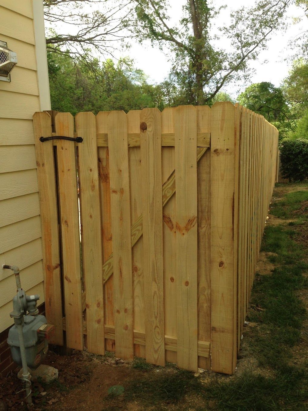 Wooden privacy fence beside a house, with a gate and outdoor utility meter.