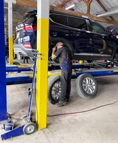 A man is working on a car on a lift in a garage.
