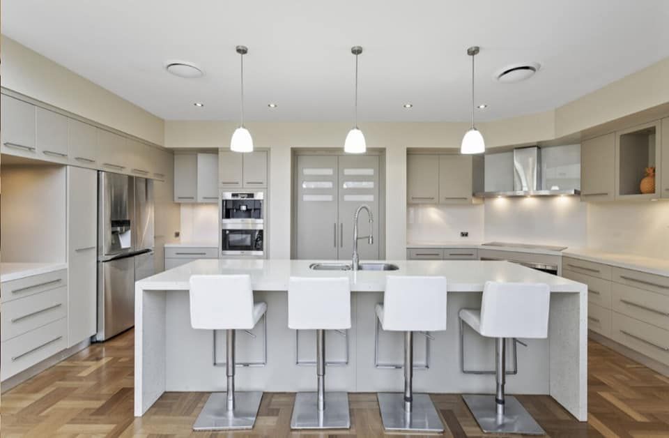 Modern kitchen with a large white island, four white bar stools, and pendant lights. — The Good Wood Polished Timber Floors in Oakey, QLD
