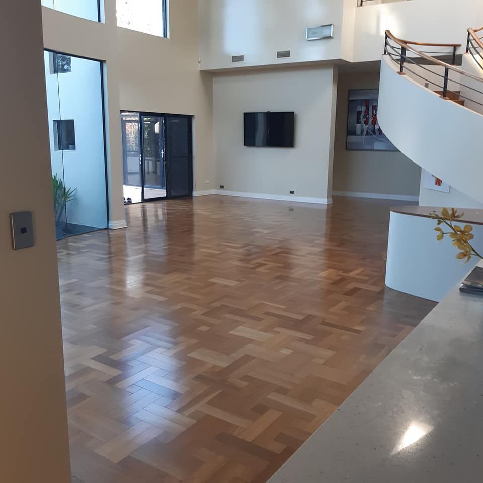 Spacious, empty living area with parquet floors, a staircase, and a mounted TV. — The Good Wood Polished Timber Floors in Pittsworth, QLD