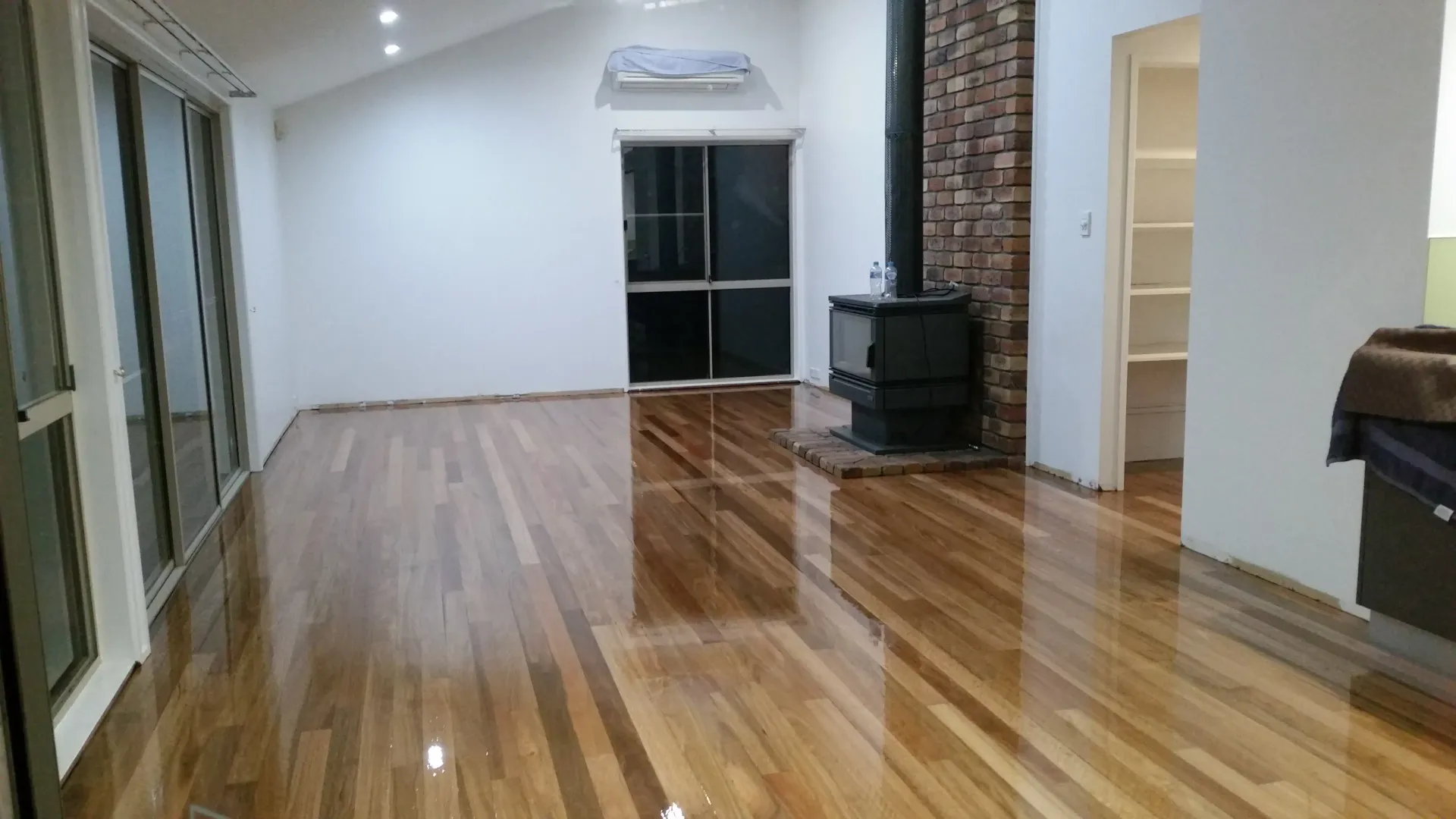 Shiny wooden floor in a living room with white walls, a fireplace, and a window. — The Good Wood Polished Timber Floors in Gatton, QLD