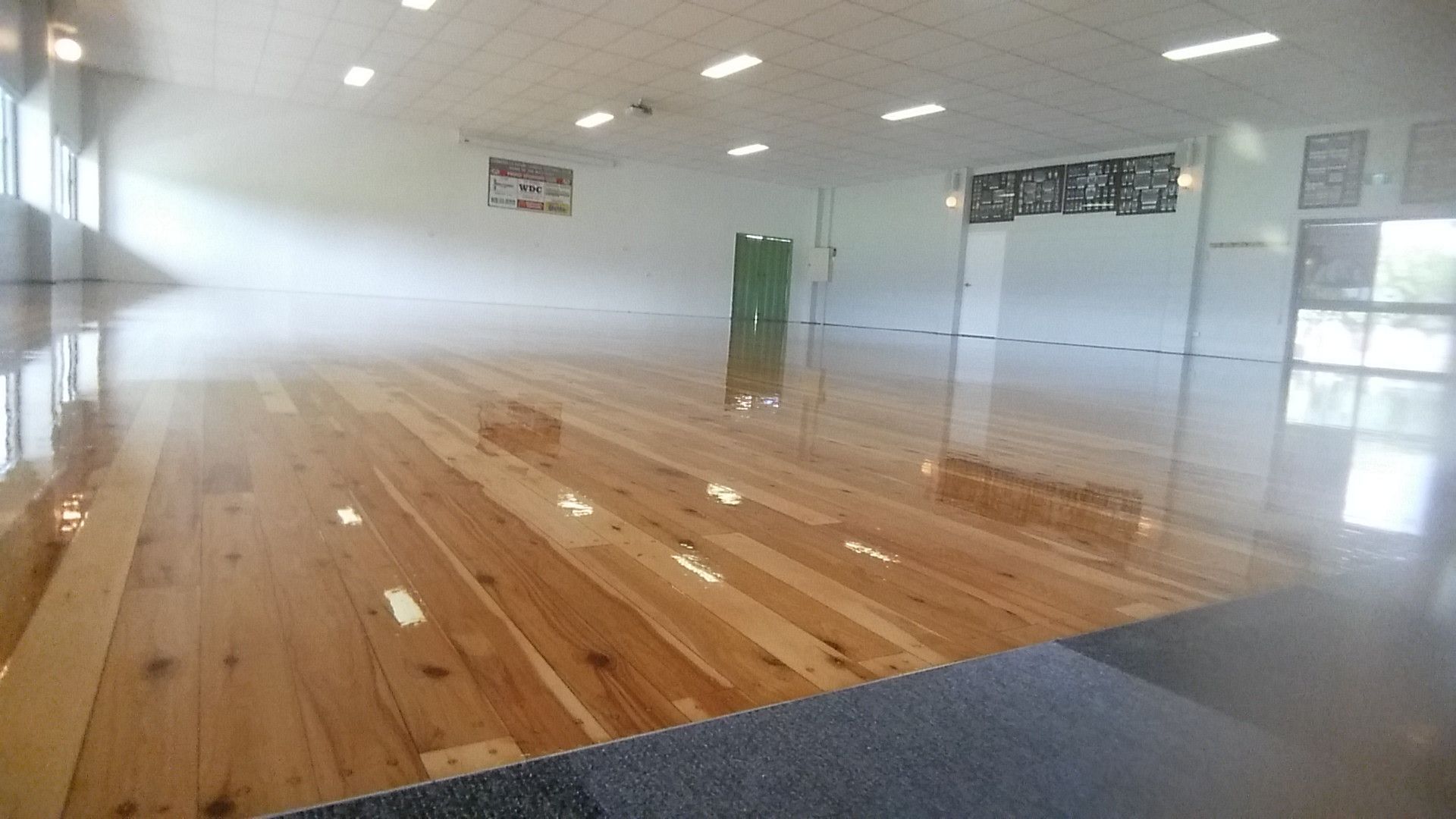 Shiny wooden floor in a well-lit interior room, with white walls and windows. — The Good Wood Polished Timber Floors in Highfields, QLD