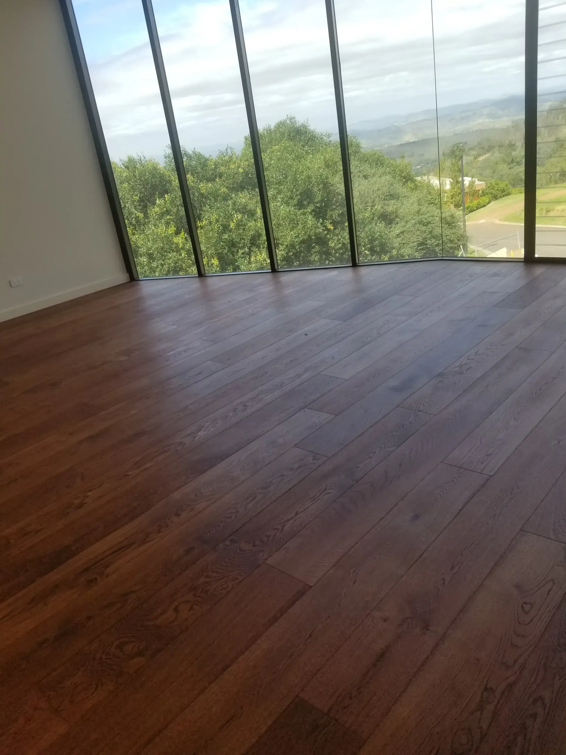 Brown wooden floor in a room with large windows overlooking a green landscape and blue sky. — The Good Wood Polished Timber Floors in Highfields, QLD