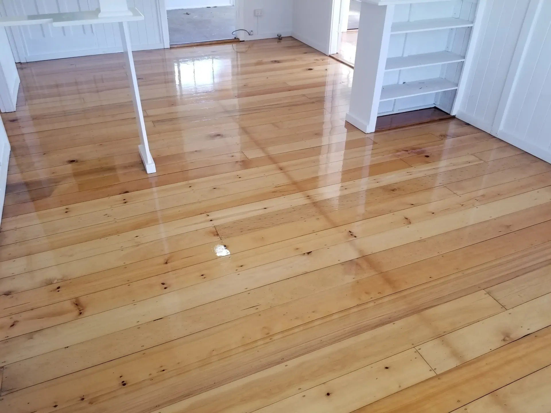 Polished wood floor in a room, reflecting light. White shelving and doorway visible. — The Good Wood Polished Timber Floors in Gatton, QLD