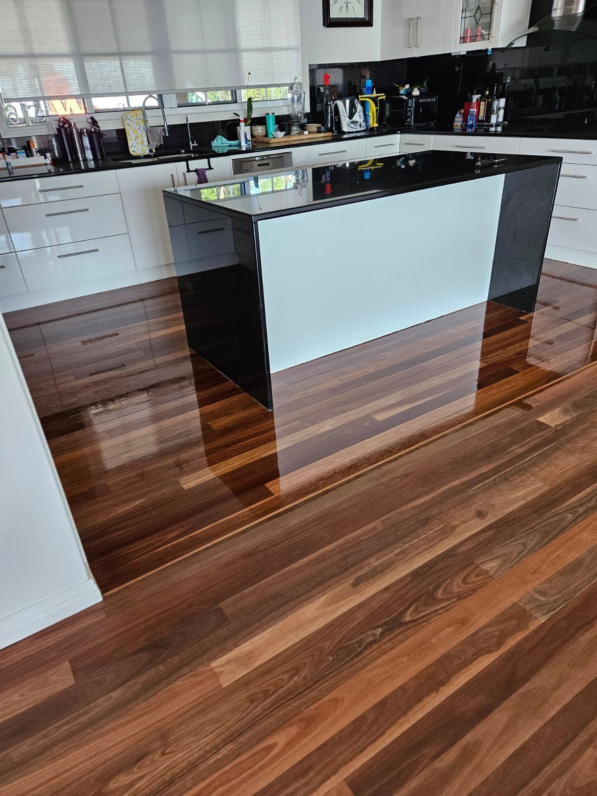 Kitchen island with black countertop and white/black sides, on wood floor. — The Good Wood Polished Timber Floors in Oakey, QLD
