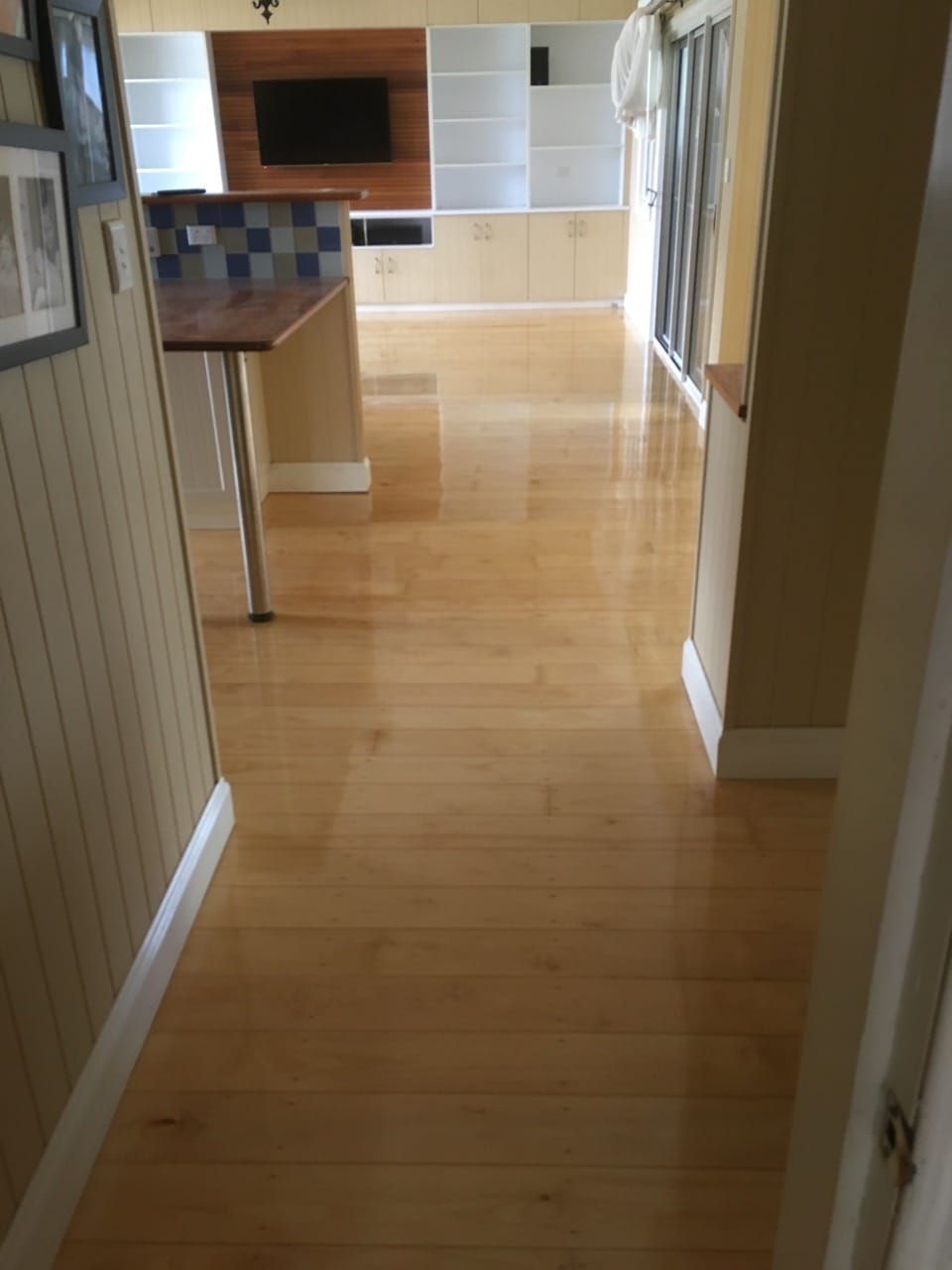 Hardwood floors in a home's hallway leading towards a kitchen, white trim, beige walls, and a wood cabinet.  — The Good Wood Polished Timber Floors in Westbrook, QLD