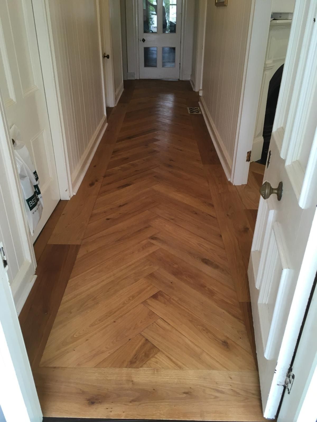 Hallway with wood herringbone flooring, white trim, and a partially open door. — The Good Wood Polished Timber Floors in Pittsworth, QLD