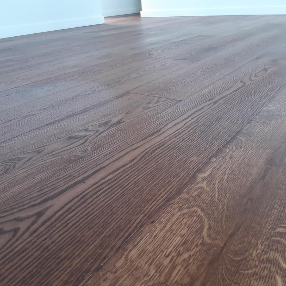 Dark hardwood floor with wood grain detail, set against a white wall. — The Good Wood Polished Timber Floors in Highfields, QLD