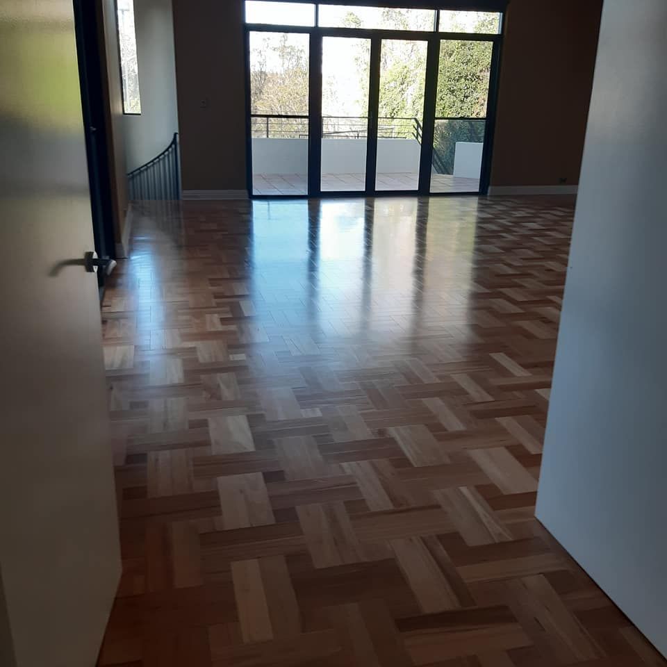 Empty room with parquet floor, glass doors to balcony, and open doorway. — The Good Wood Polished Timber Floors in Gatton, QLD