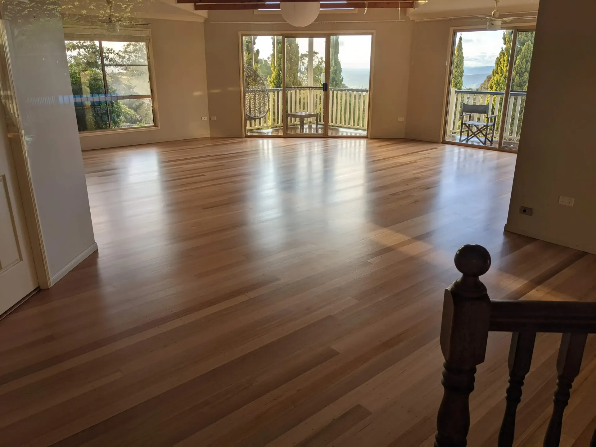 Empty room with polished wooden floor and glass doors opening to a balcony with a scenic view. — The Good Wood Polished Timber Floors in Gatton, QLD