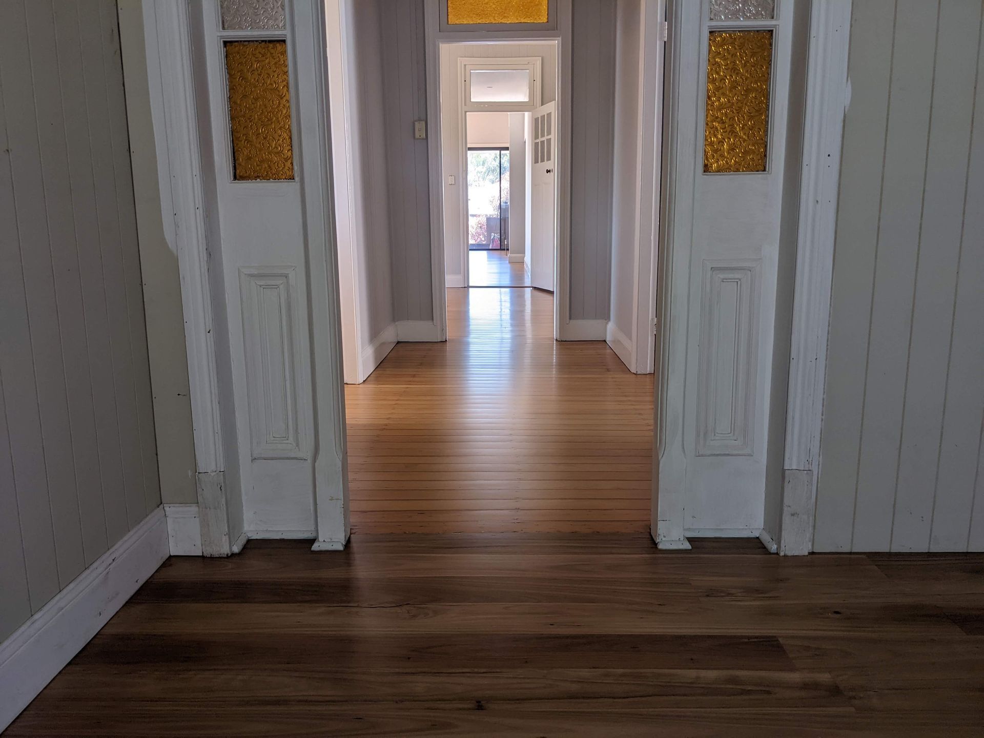 Wooden hallway with open doorways, featuring white trim, stained glass, and light reflecting from the wooden floor.