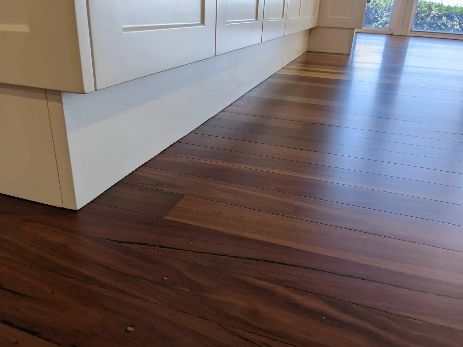 Dark wood floor next to white kitchen cabinets. — The Good Wood Polished Timber Floors in Gatton, QLD