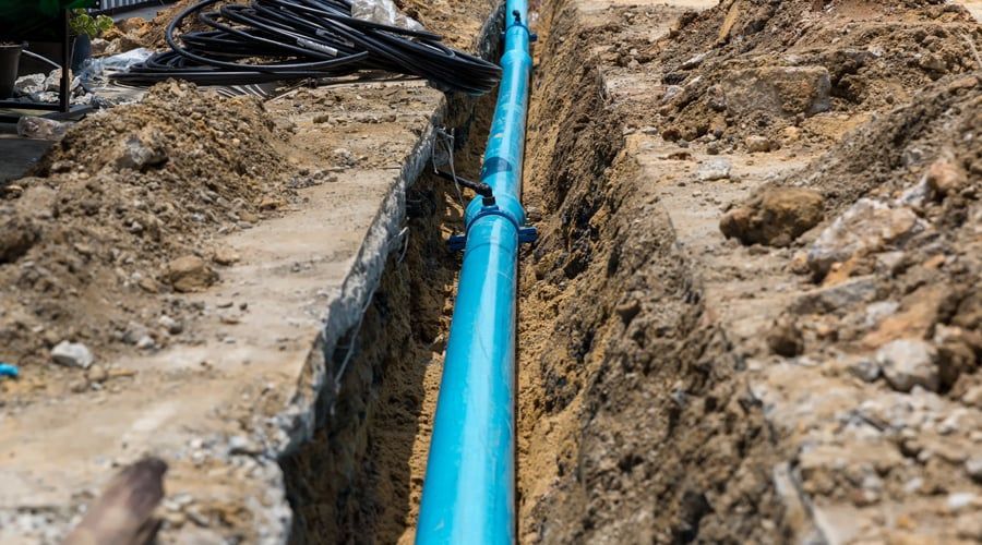 A blue pipe is being installed in a trench.