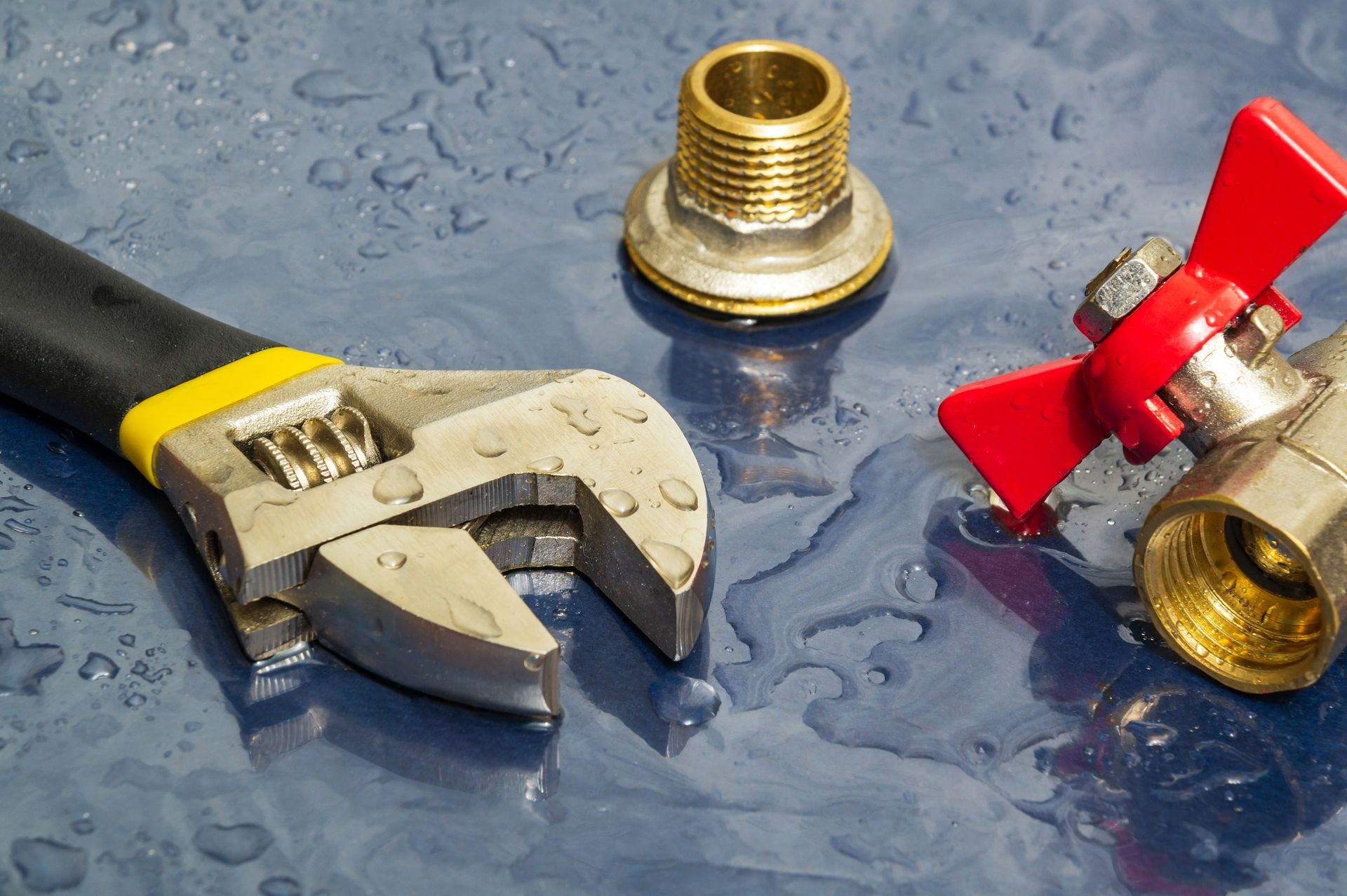 A wrench and a valve are sitting on a wet surface.
