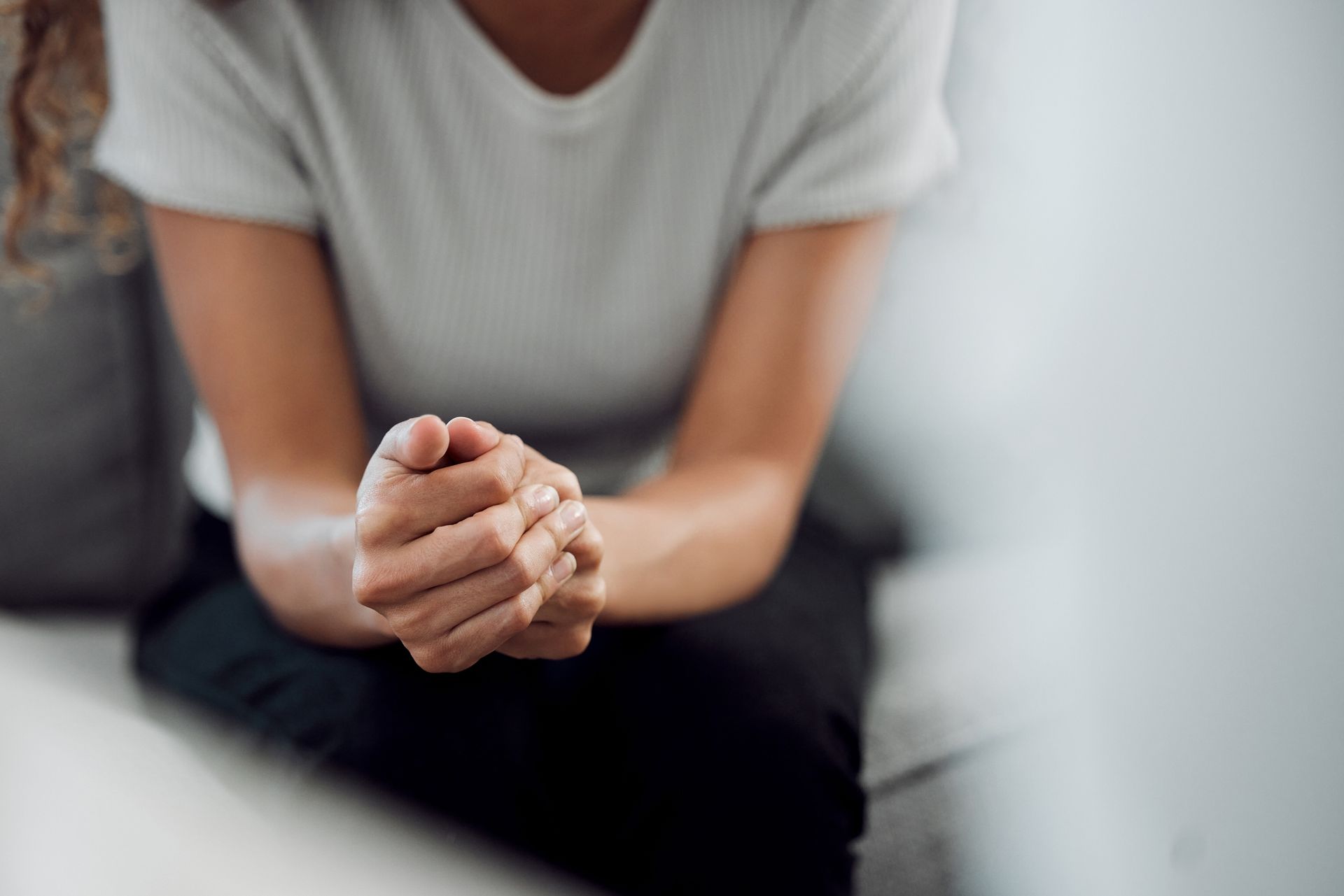 A woman is sitting on a couch with her hands folded in prayer.