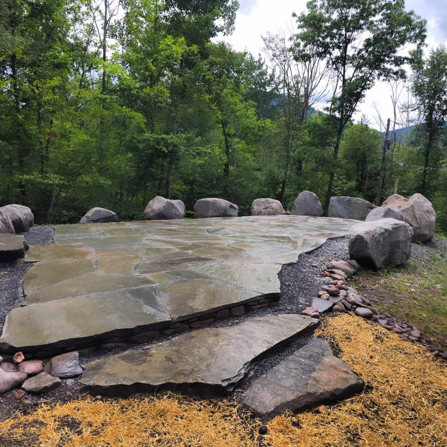 A large stone patio in the middle of a forest with trees in the background.