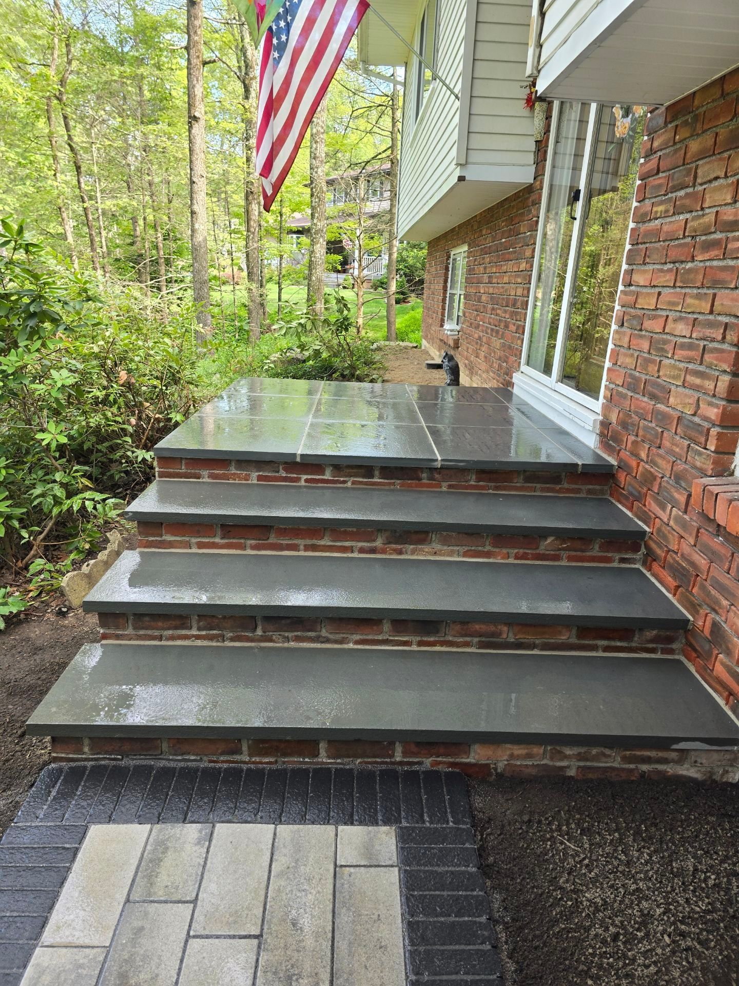 A set of stairs leading up to a brick house with an american flag flying in the background.