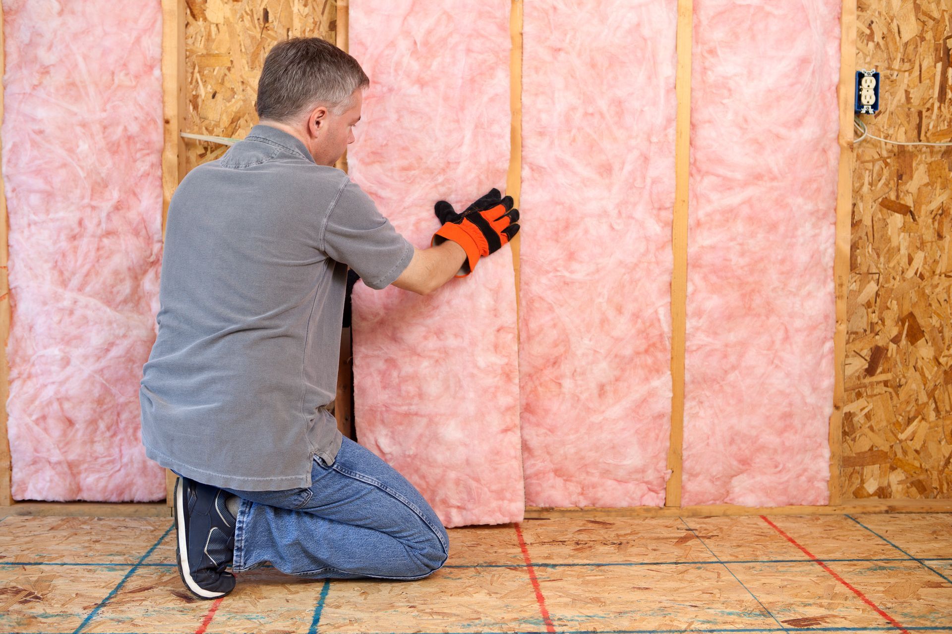A man is kneeling down while installing insulation on a wall.
