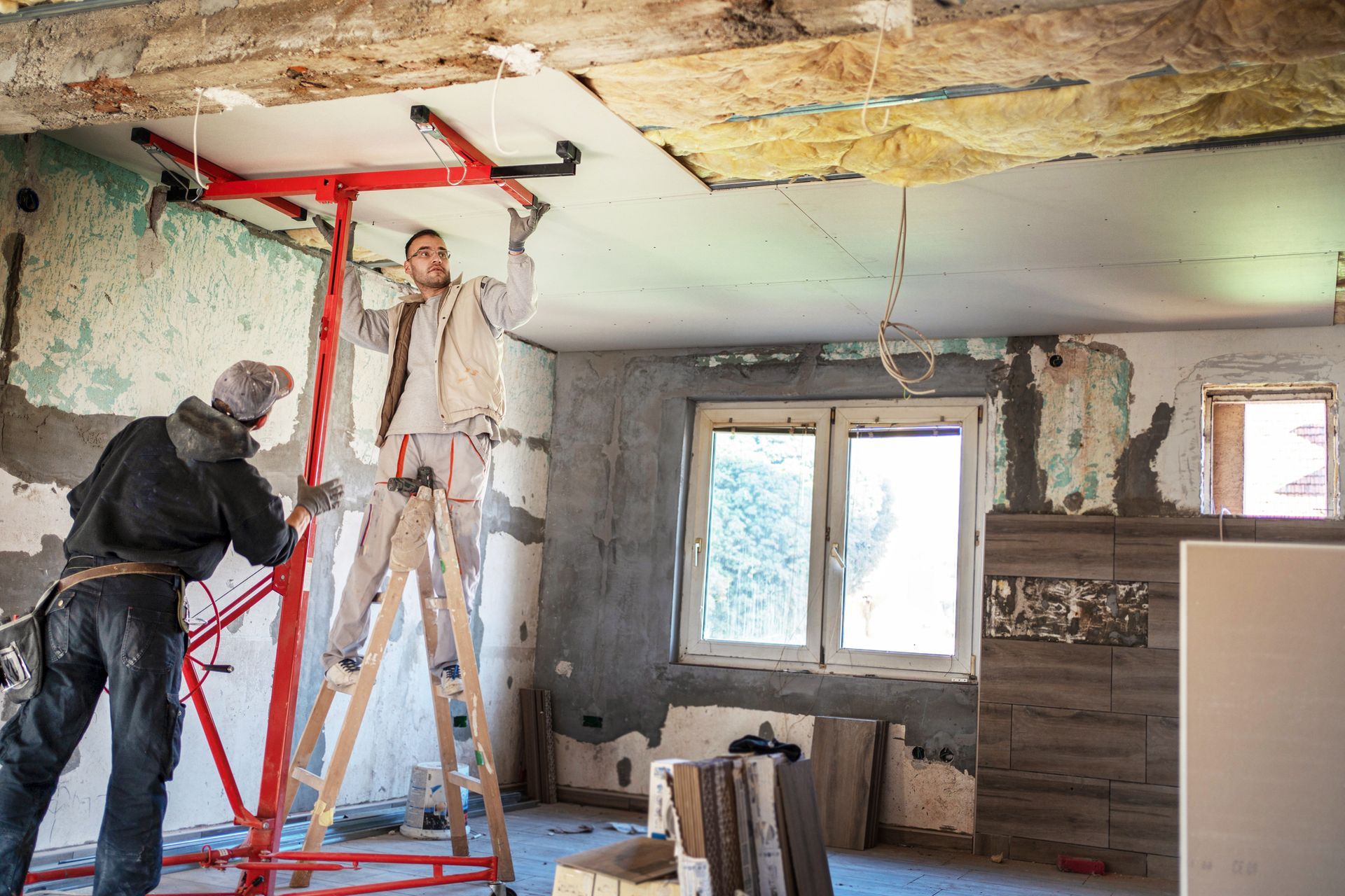 Two men are working on a ceiling in a room.