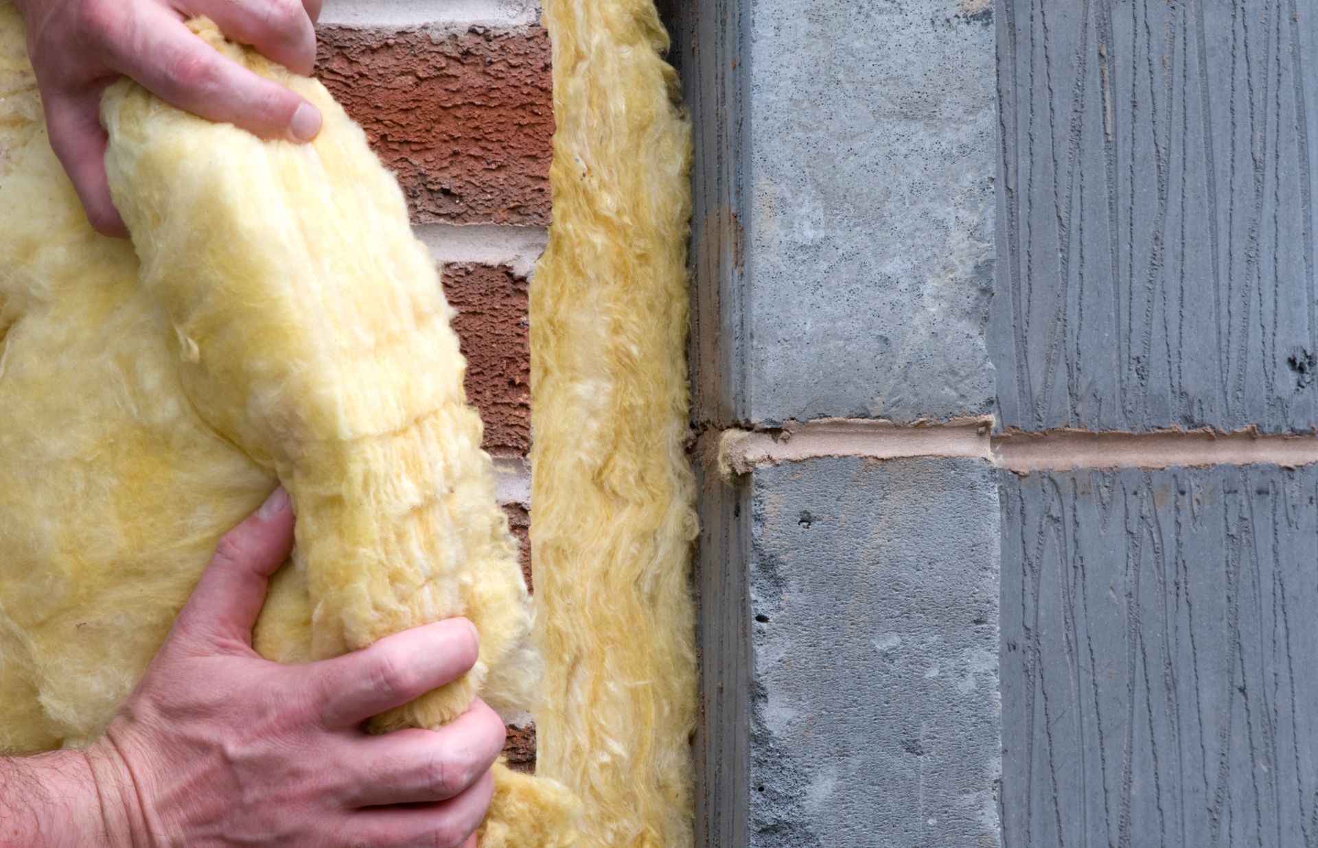 A person is holding a piece of insulation on a brick wall.