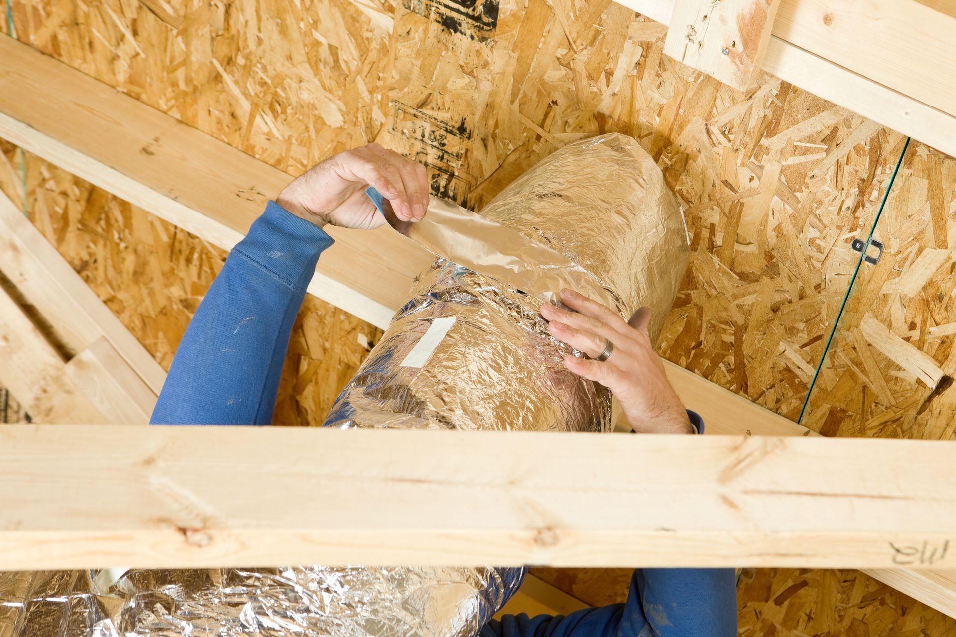 A person is working on a duct in the attic of a house.