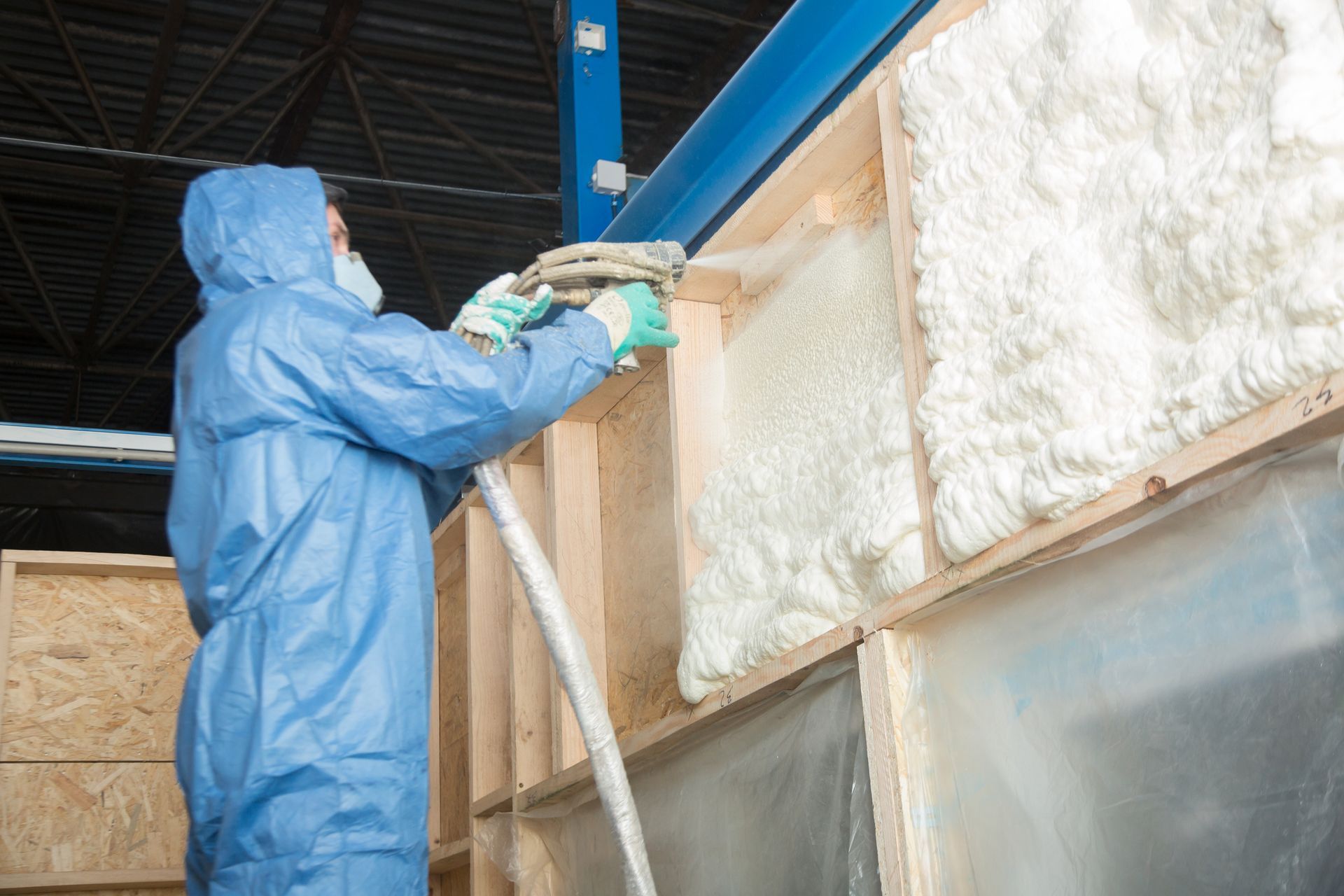 A man in a blue suit is spraying foam on a wall.