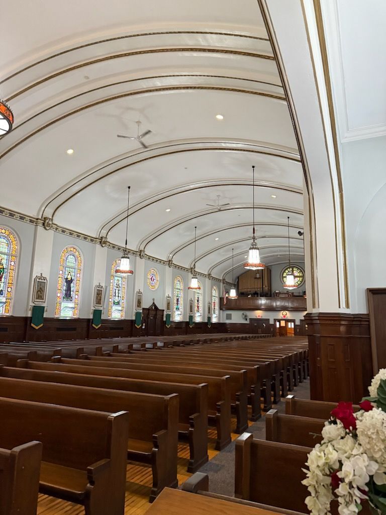 The inside of a church with rows of wooden benches and stained glass windows.