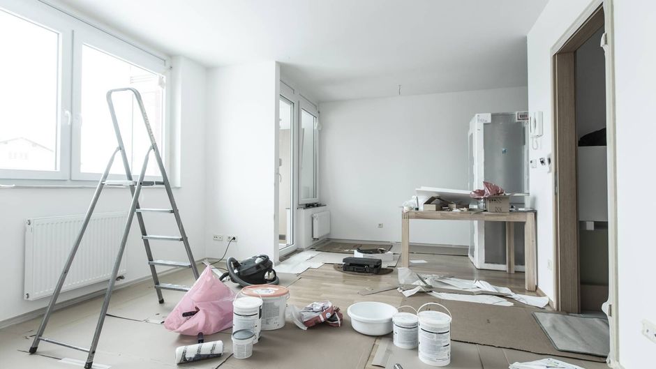 An empty room with a ladder and buckets of paint on the floor.