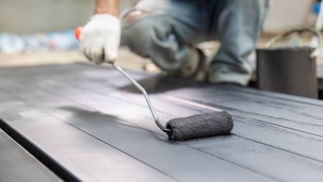 A person is painting a wooden surface with a roller.