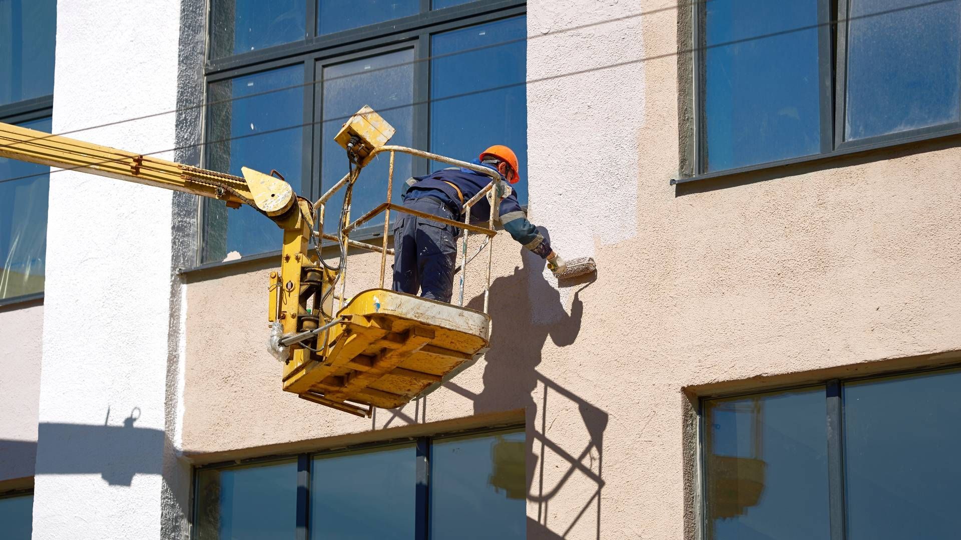 A man is cleaning the windows of a building with a crane.